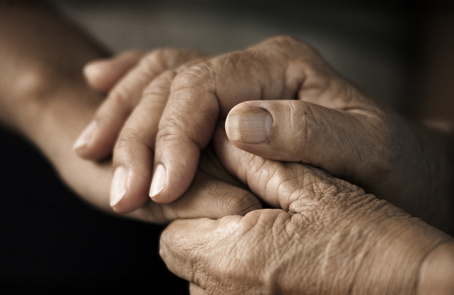 Foto mostra mãos de pessoa idosa segurando a mão de uma outra pessoa.
