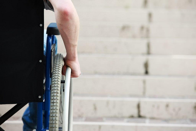 Foto mostra apenas o braço direito de um hoimem segurando a roda de uma cadeiras de rodas, com uma escada não acessível á sua frente.