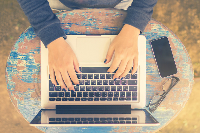 Girl sits at a table with a laptop and cell phone