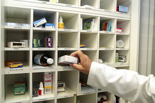 Foto de médico pegando medicamento em uma prateleira com escaninhos e diversos medicamentos diferentes.