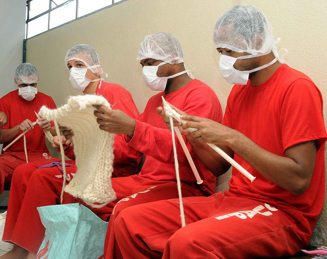 Presos fazendo tricô usando máscaras e toucas descartáveis