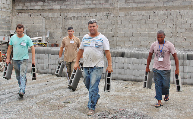 Presos segurando blocos de concreto feitos por eles