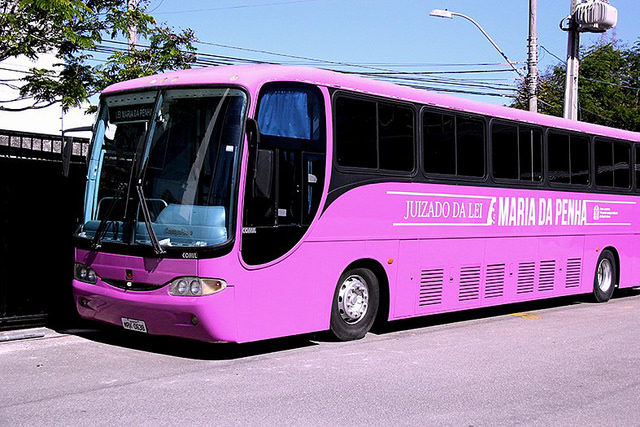 Foto mostra um ônibus rosa estacionado, onde se lê, na lateral, "Juizado da Lei Maria da Penha".