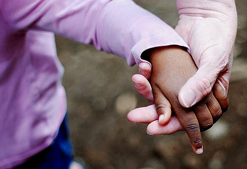 Foto mostra a mão de uma mulher branca segurando a mão de uma criança negra.