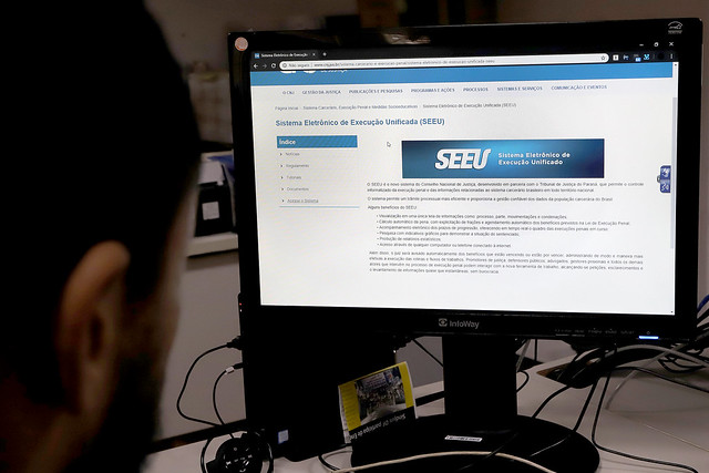 Foto de uma mulher sentada de costas, olhando para a tela do cpmputador com a tela de acesso ao SEEU