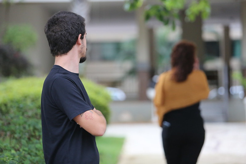Imagem de homem em via pública, em primeiro plano, observando mulher de costas