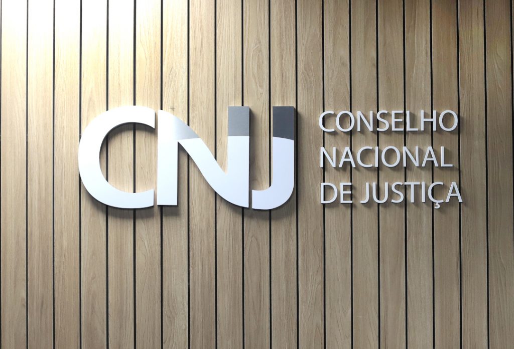 Foto da logomarca do CNJ dentro do auditório, onde se lê CNJ, Conselho Nacional de Justiça