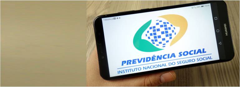 Foto mostra um hjomem segurando um celular e na tela se vê a logomarca da Previdência Social.
