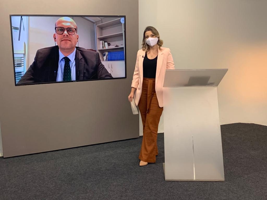 Foto da apresentadora Mariana xavier no estúdio de gravação do programa, tendo ao fundo um telão com a imagem do entrevistado Antonio Carlos Tavares, juiz auxiliar da Presidência do CNJ