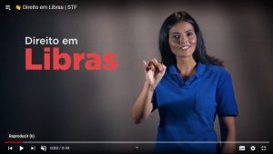 Frame de vídeo da série Direito em Libras, com o nome do projeto e uma mulher vestida de azul fazendo sinal em Libras