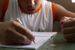 Foto de adolescente escrevendo em um caderno. O adolescente está em unidade de internação socioeducativa, em Aracaju (SE)