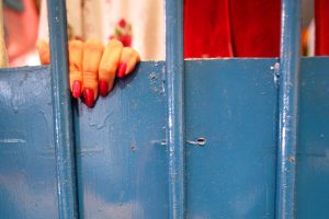 Foto de mão feminina, com as unhas pintadas, segurando as grades da prisão