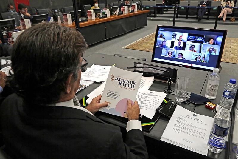 Foto do ministro Luiz Fux, presidente do CNJ, com o relatório do GT de Igualdade Racial no Judiciário, participando de reunião por videoconferência.