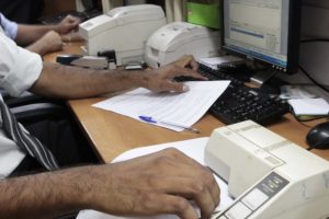 Foto de atendente em cartório registrando autenticação em cópia de documento.