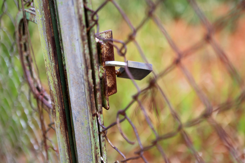 Foto ilustrativa de obra parada, com um cadeado fechando um portão