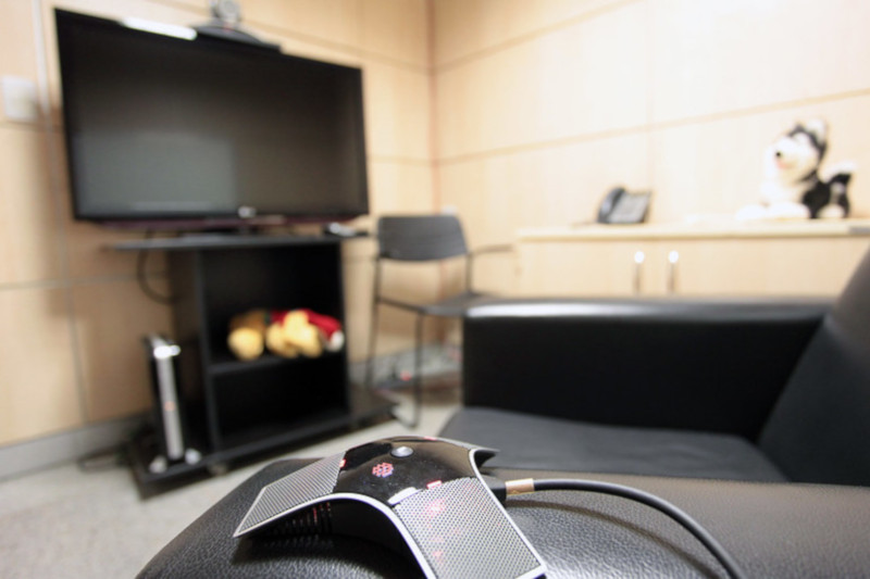 Foto mostra sala de depoimento especial do TJDFT, onde ao fundo, fora de foco, é possível ver uma cadeira, uma estante com um aparelho de telefone e um bicho de pelúcia em cima e uma TV 42" em um rack. Em destaque, à frente da foto e com foco, está um controle de videogame.