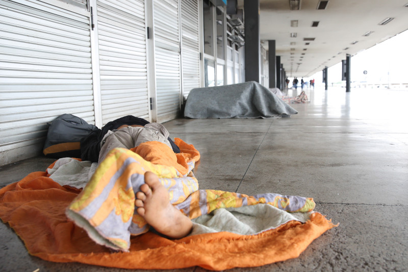 Foto de pessoa em situação de rua deitado no chão em um corredor de espaço comercial em Brasília
