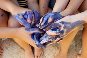 Foto mostra diversas mãos de crianças entrelaçadas e sujas de tinta.
