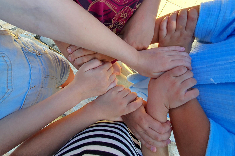Foto de mãos de crianças, com uma segurando o braço da outra em uma brincadeira.