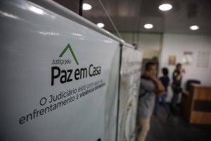 Foto mostra um banner exposto em um ambiente fechado, onde se lê: "Justiça pela Paz em Casa. O Judiciário está com você no enfrentamento à violência doméstica".