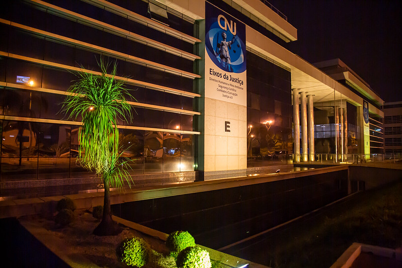 Foto noturna da fachada da sede do Conselho Nacional de Justiça (CNJ), em Brasília. Em destaque em uma das paredes, um banner que destaca os Eixos da Justiça trabalhados na gestão do ministro Luiz Fux (2020-2022).