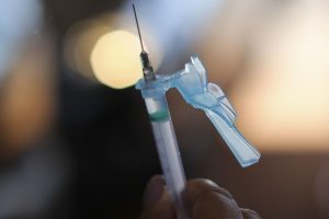 Foto mostra mão de uma pessoa segurando uma seringa aplicadora de vacina.