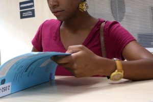 Foto mostra uma mulher negra olhando um processo em um balcão.