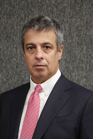 Foto do conselheiro do CNJ Mauro Martins. Ele está usando paletó preto, camisa branca e gravata rosa, em frente a um fundo texturizado cinza.