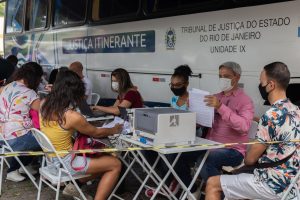 Foto mostra o ônibus da Justiça Itinerante, com as pessoas sendo atendidas durante ação de requalificação civil para pessoas não-binárias e transexuais.