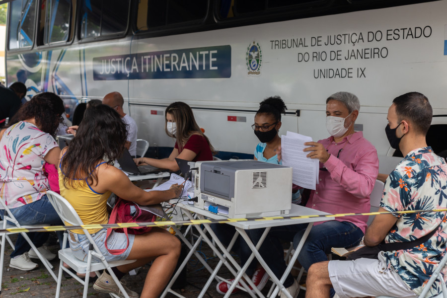 Foto mostra o ônibus da Justiça Itinerante, com as pessoas sendo atendidas durante ação de requalificação civil para pessoas não-binárias e transexuais.