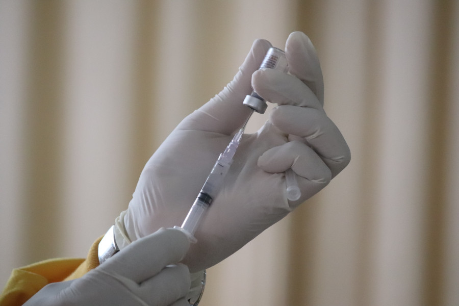 Foto de uma pessoa usando luvas de borracha que está preenchendo uma seringa com uma dose de vacina contra a Covid-19.