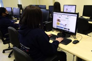 Foto mostra 3 jovens sentadas em frente a computadores em uma atividade do projeto.