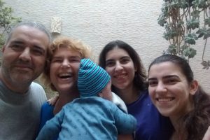 Foto mostra Lumena e o marido abraçados e sorrindo com duas adolescentes e uma criança recém-nascida.