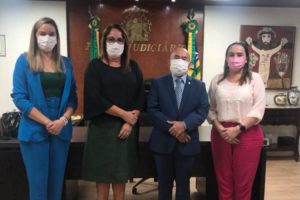 Foto mostra os quatro participantes da reunião no TJPI em pé, posando em frente à mesa do presidente do Tribunal.