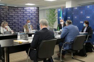 Foto mostra momento da reunião, com participantes sentados em volta de uma mesa em U. Ao fundo, backdrops com a logomarca do CNJ.