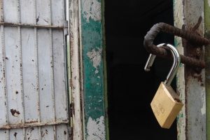 Foto mostra uma porta de prisão aberta com um cadeado, também aberto, pendurado.