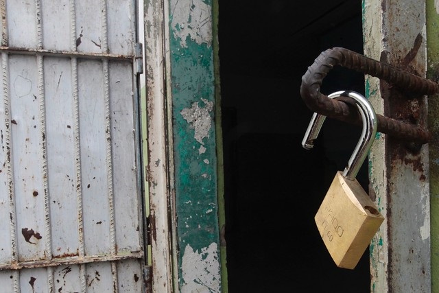 Foto mostra uma porta de prisão aberta com um cadeado, também aberto, pendurado.