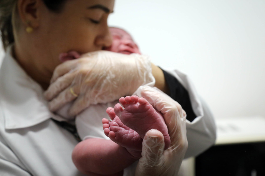 Foto mostra enfermeira segurando criança recém-nascida.