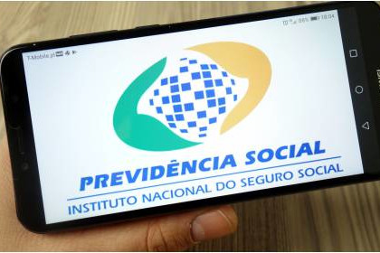Foto mostra um hjomem segurando um celular e na tela se vê a logomarca da Previdência Social.