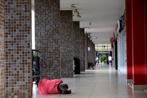 Foto de pessoa em situação de rua deitado no chão em um corredor de espaço comercial em Brasília