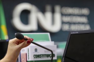 Foto mostra a mão de uma mulher segurando o microfone dentro do Plenário do CNJ.