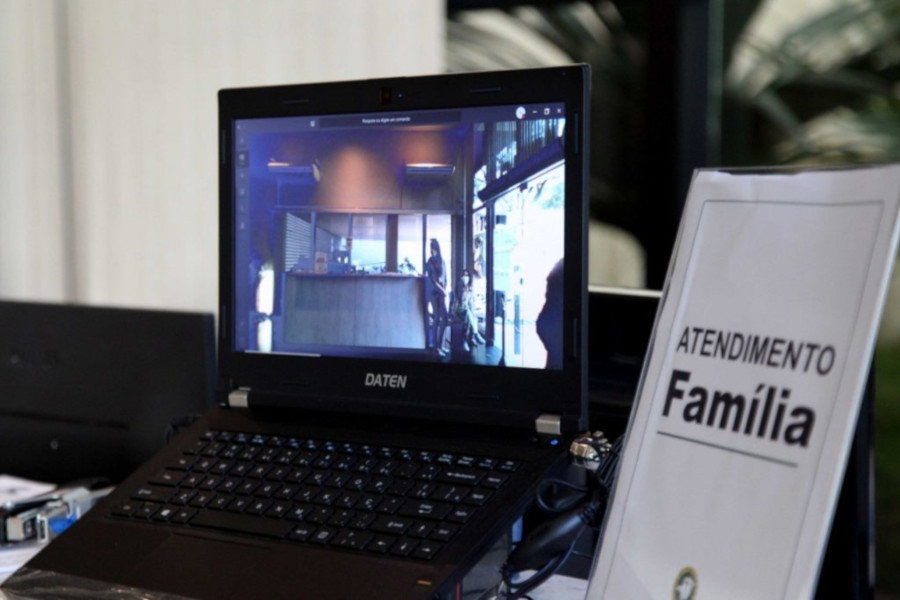 Foto mostra um notebook em uma estação de trabalho. Ao lado, tem uma placa sinalizadora com o texto "Atendimento Família".