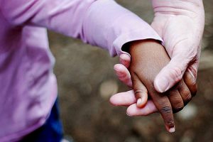 Foto mostra a mão de uma mulher branca segurando a mão de uma criança negra.