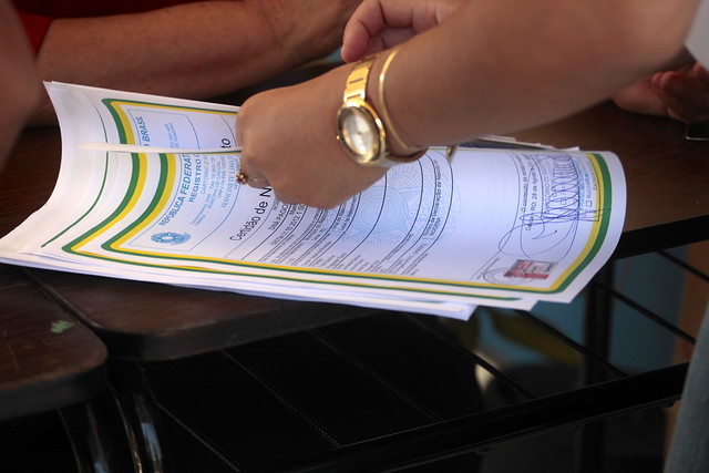 Foto mostra as mãos de uma pessoa mexendo em uma pequena pilha de Certidões de Nascimento.