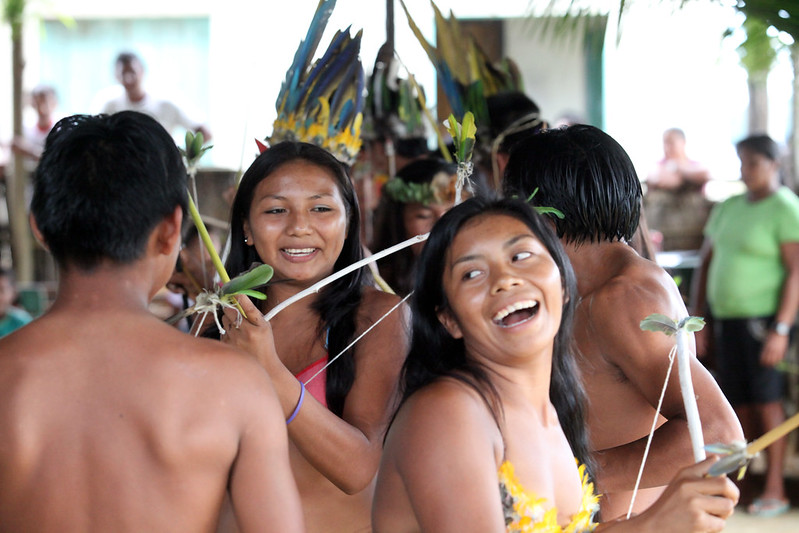 Foto mostra cerimônia de dança em comunidade indígena na região do Alto Rio Negro, no Amazonas, com destaque a duas mulheres indígenas sorrindo.