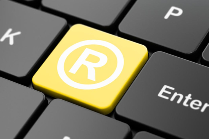 Foto mostra um teclado de computador e uma das teclas está destacada em amarelo com o símbolo de marca registrada nela ao invés de uma letra.