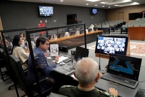 Foto do Plenário do CNJ durante a reunião, com o conselheiro Bandeira falando para o telão onde estão as pessoas participando por videoconferência.