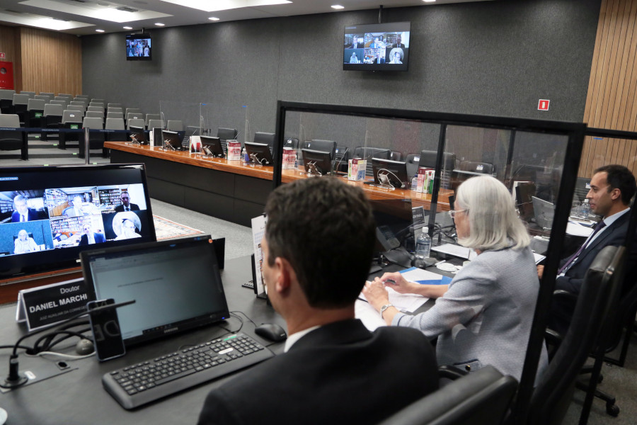 Foto mostra a bancada de coordenadores do grupo de trabalho no Plenário do CNJ. A foto mostra a corregedora nacional de Justiça e os ministros do STJ sentados, de costas, enquanto olham para o telão no centro do Plenário com as demais pessoas participantes por videoconferência.