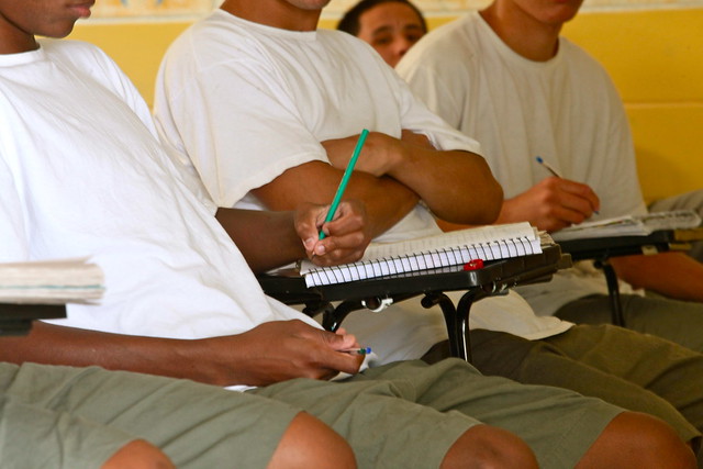 Foto mostra jovens sentados em carteiras de sala de aula, com cadernos e canetas, em unidade do sistema socioeducativo.