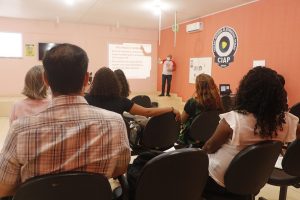 Foto mostra momento da capacitação na sala do CIAP, estando o apresentador na frente da sala e diversas pessoas sentadas assistindo.